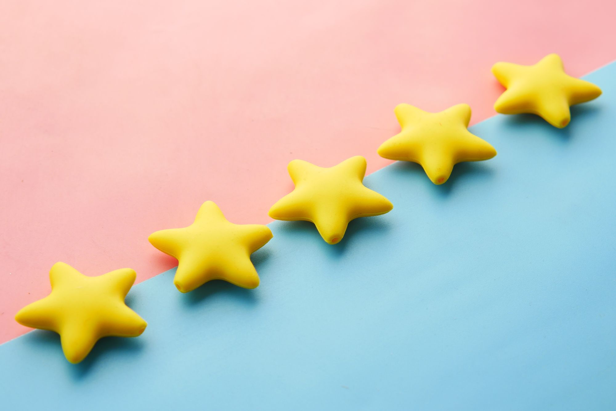 Fünf gelbe Sterne liegen diagonal auf rosa und blauem Hintergrund als Symbol für Kundenbewertungen